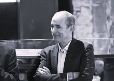 Photo d'un homme souriant, avec une tenue professionnelle chemise blanche et blazer noir, croisant les bras
